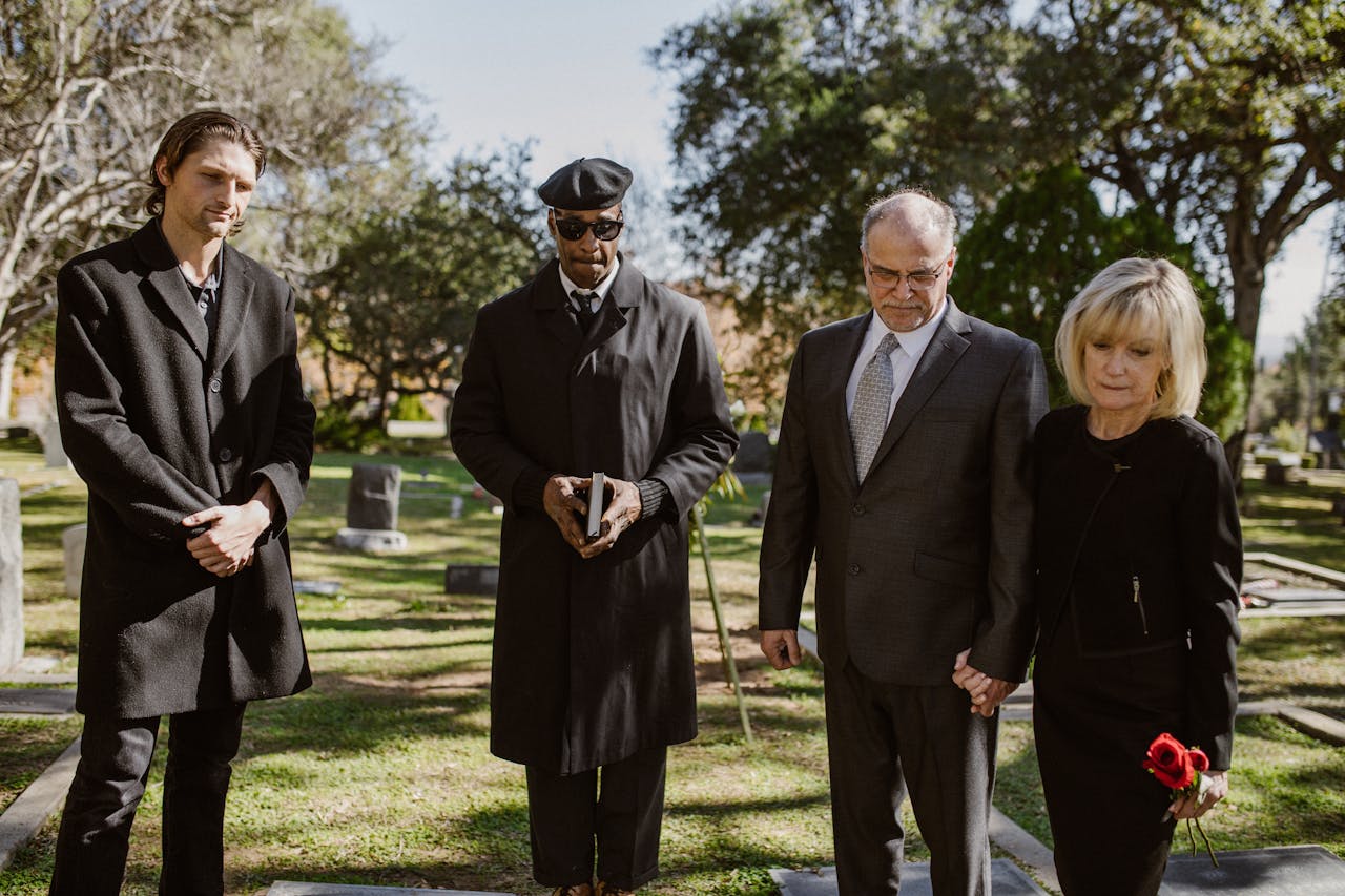 Home A diverse group attending a memorial service in a serene graveyard setting.